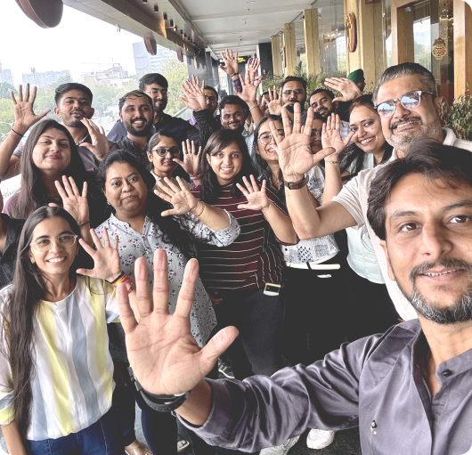 Group selfie of the Movegistics 5.0 engineering team smiling and waving at the camera outdoors.